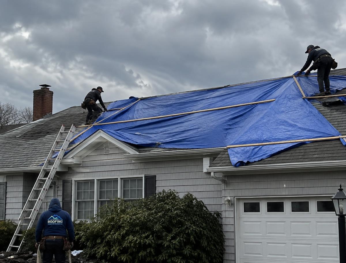 NB Construction crew installing a heavy-duty blue emergency tarp over a storm-damaged Long Island roof